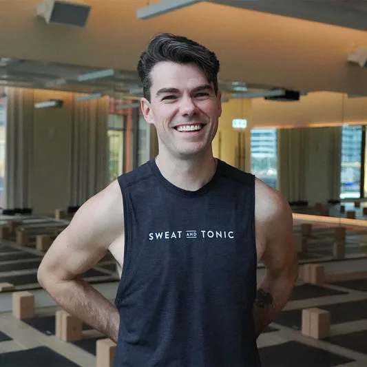 A smiling man in a fitness studio wearing a Sweat and Tonic shirt.