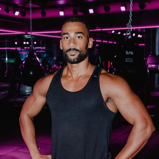 A muscular man in a fitness studio with pink lighting.