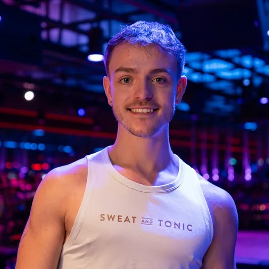 A smiling man in a fitness studio wearing a tank top.