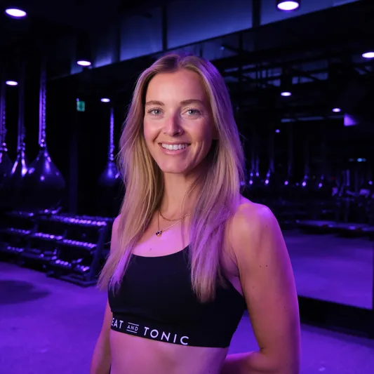 Smiling woman in fitness studio wearing 'Sweat and Tonic' attire.
