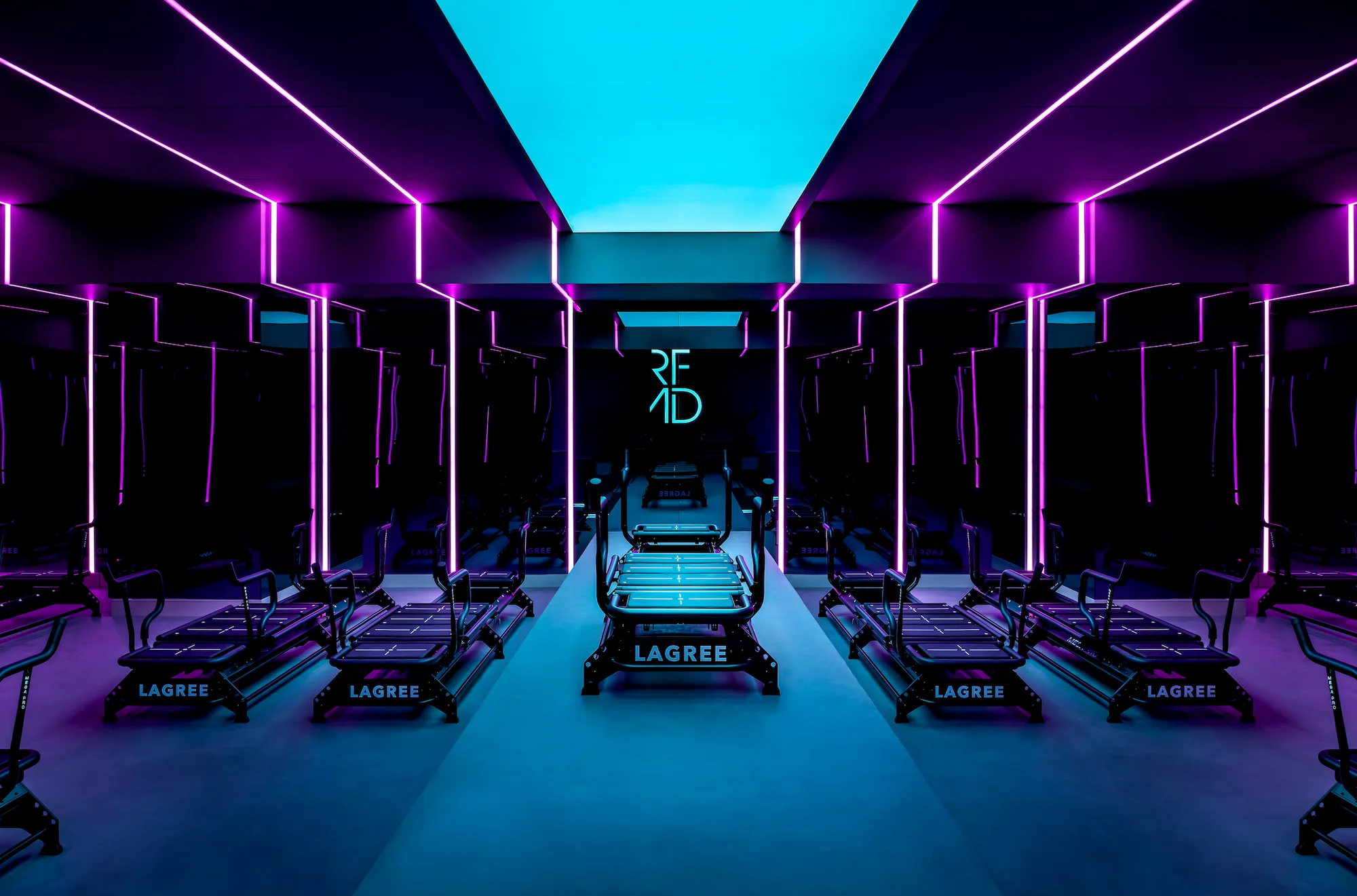 A modern fitness studio with Lagree machines and neon lighting.