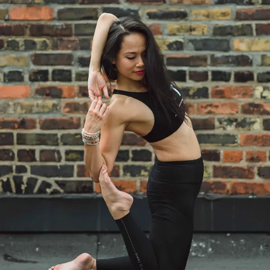 A woman in a yoga pose against a brick wall.