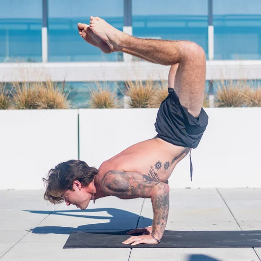 A man performing a yoga pose outdoors on a mat.