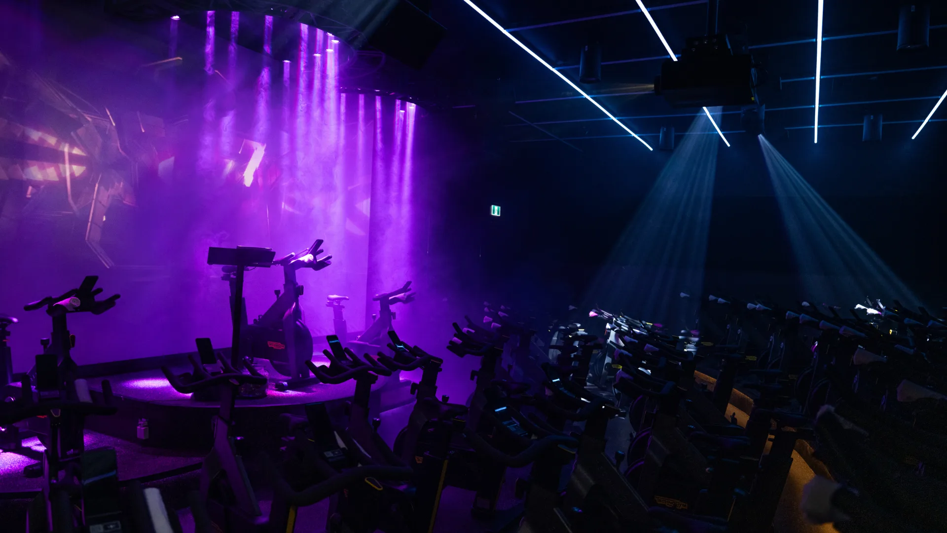 Indoor cycling studio with purple lighting and stationary bikes.