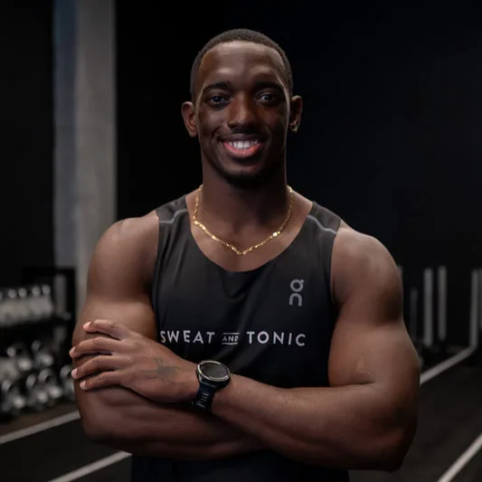A smiling man in a fitness studio wearing a tank top.
