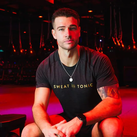 A man in a Sweat and Tonic shirt poses in a gym.