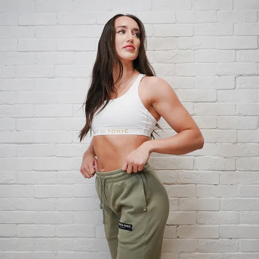 A woman in activewear poses against a brick wall.