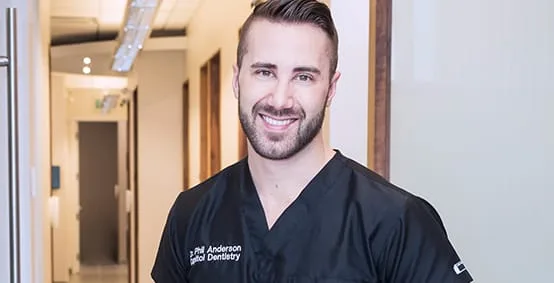A dentist smiling in a modern dental office hallway.