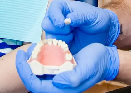 Hands holding a dental implant and mouth model at a dental office.