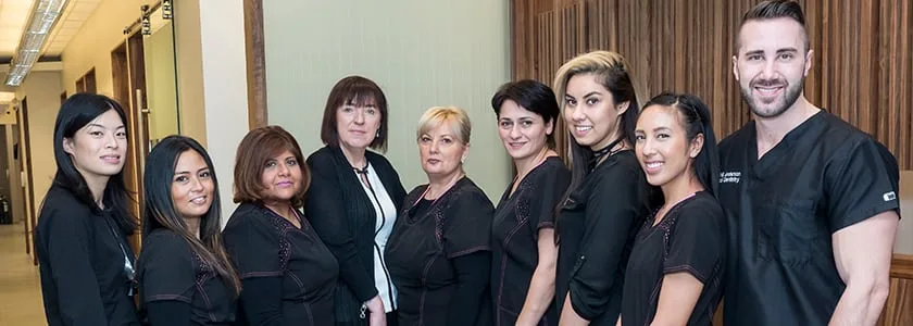 A diverse dental team in black scrubs standing in their office.