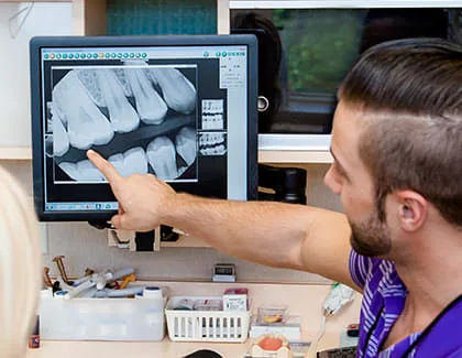A dental professional examines an X-ray on a computer screen.