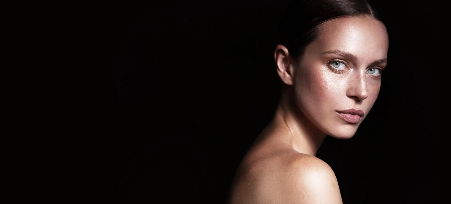 A woman with clear skin and striking blue eyes against a dark background.