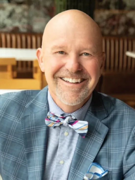 A man smiling in a checked suit and bow tie.