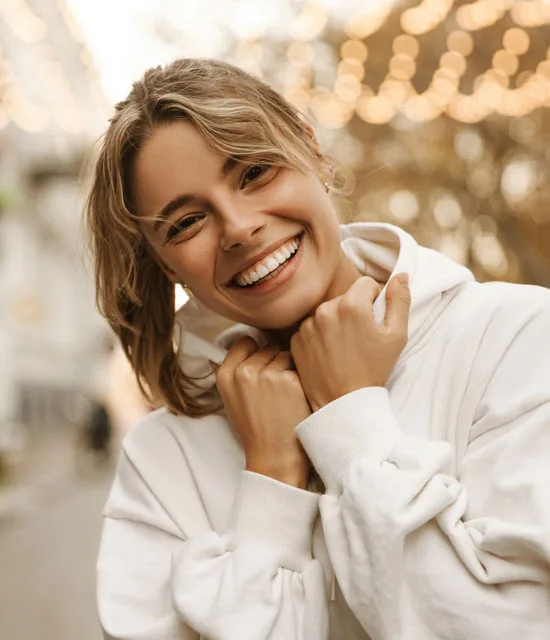 A smiling young woman in a white hoodie outdoors.